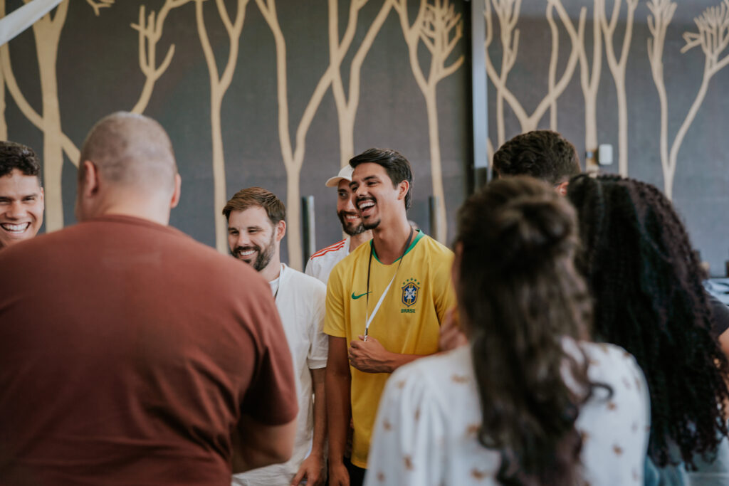 Gruppen junger Menschen beim positiven Austausch in einem modernen Raum, inklusive eines Brasilien-Feldesports-Trikots, symbolisiert Gemeinschaft, Freude und internationale Verbundenheit.