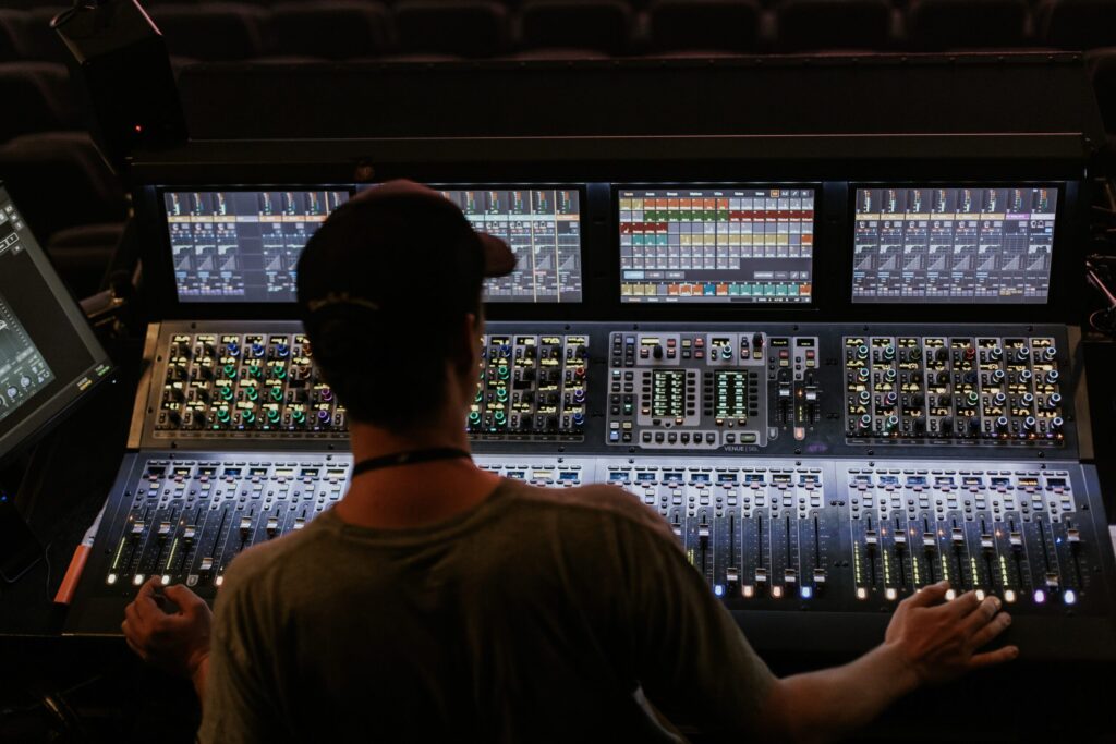 Benutzer steuert ein großes digitales Mischpult mit mehreren Bildschirmen, Tasten und Reglern.