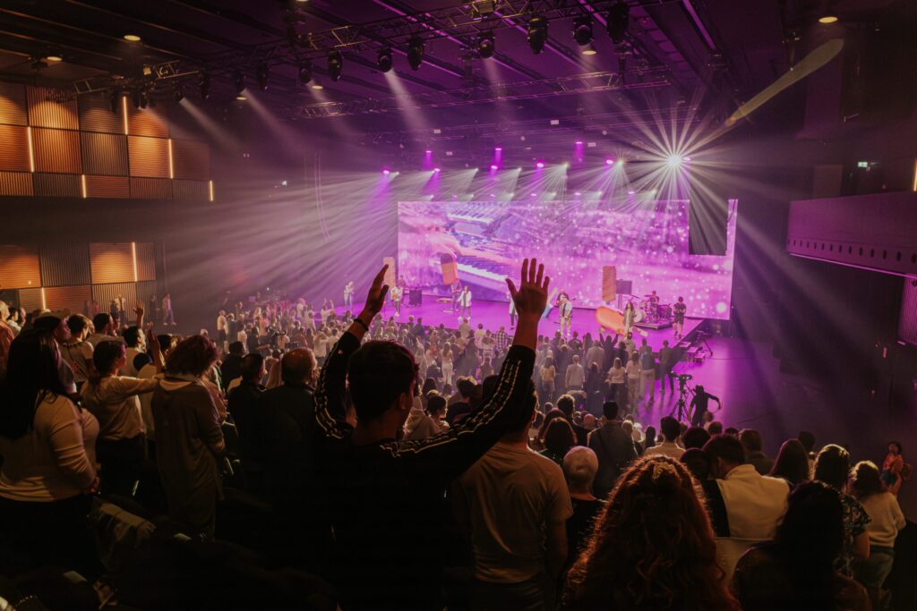 Eine große Bühne mit einer bunten, leuchtenden LED-Wand im Hintergrund, Musiker performen.