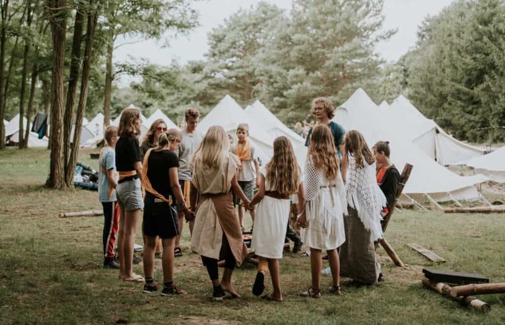 Menschen um ein Lagerfeuer bei einem Outdoor-Camp, umgeben von Zelten im Wald, Gemeinschaft und Freizeitaktivitäten, ideal für Familien- oder Jugendcamp in Mannheim.