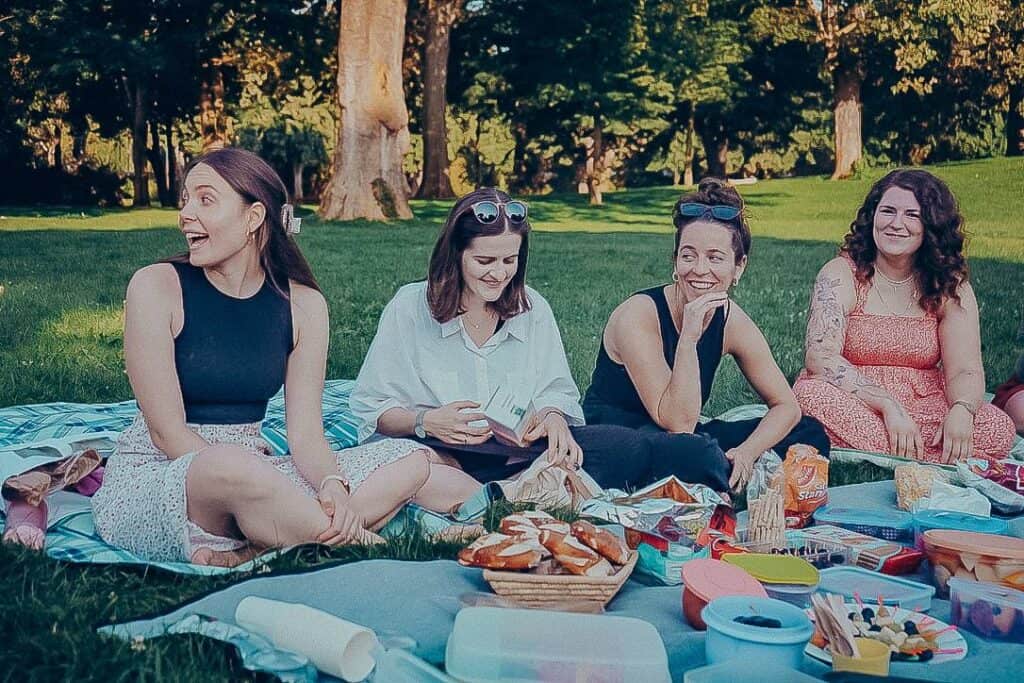 Entspannte Frauen beim Picknick im Park, lachen und genießen Gemeinschaft mit Freunden, symbolisiert Freude, Zusammengehörigkeit und einen positiven Gemeinschaftsgeist bei ICF Mannheim.
