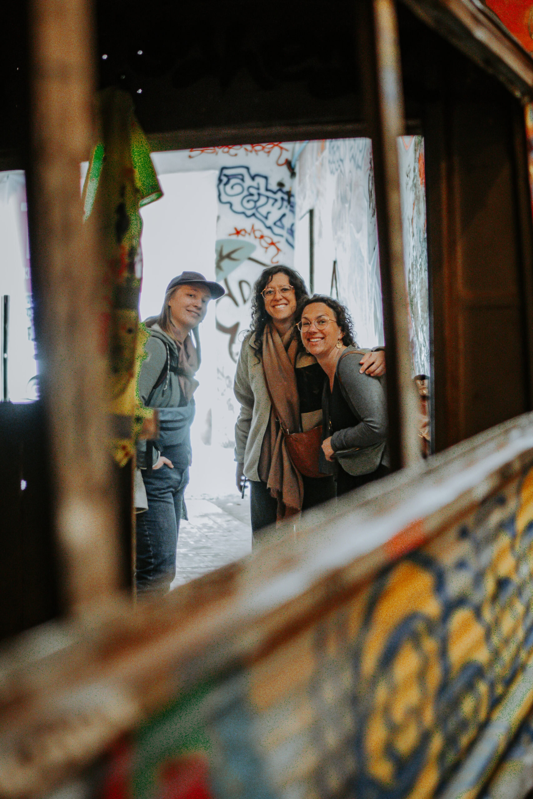 Drei Frauen stehen vor einer Wand mit Graffiti, lachen und unterhalten sich.