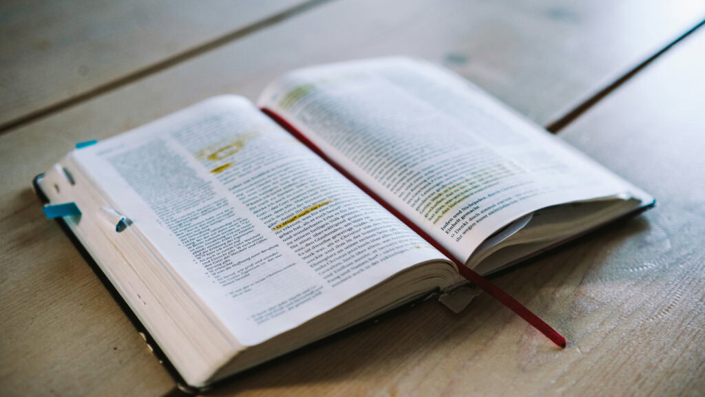 Geöffnete Bibel mit Lesezeichen auf Holztisch.