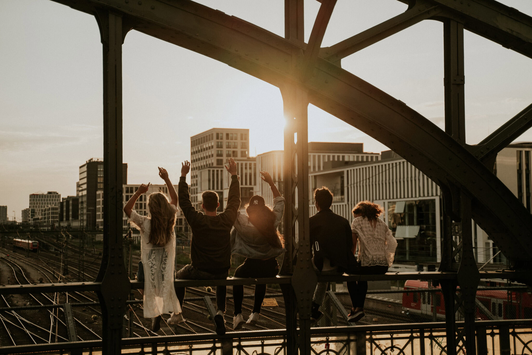 Menschen sitzen auf einer Brüstung unter einer Brücke, Sonnenlicht im Hintergrund.