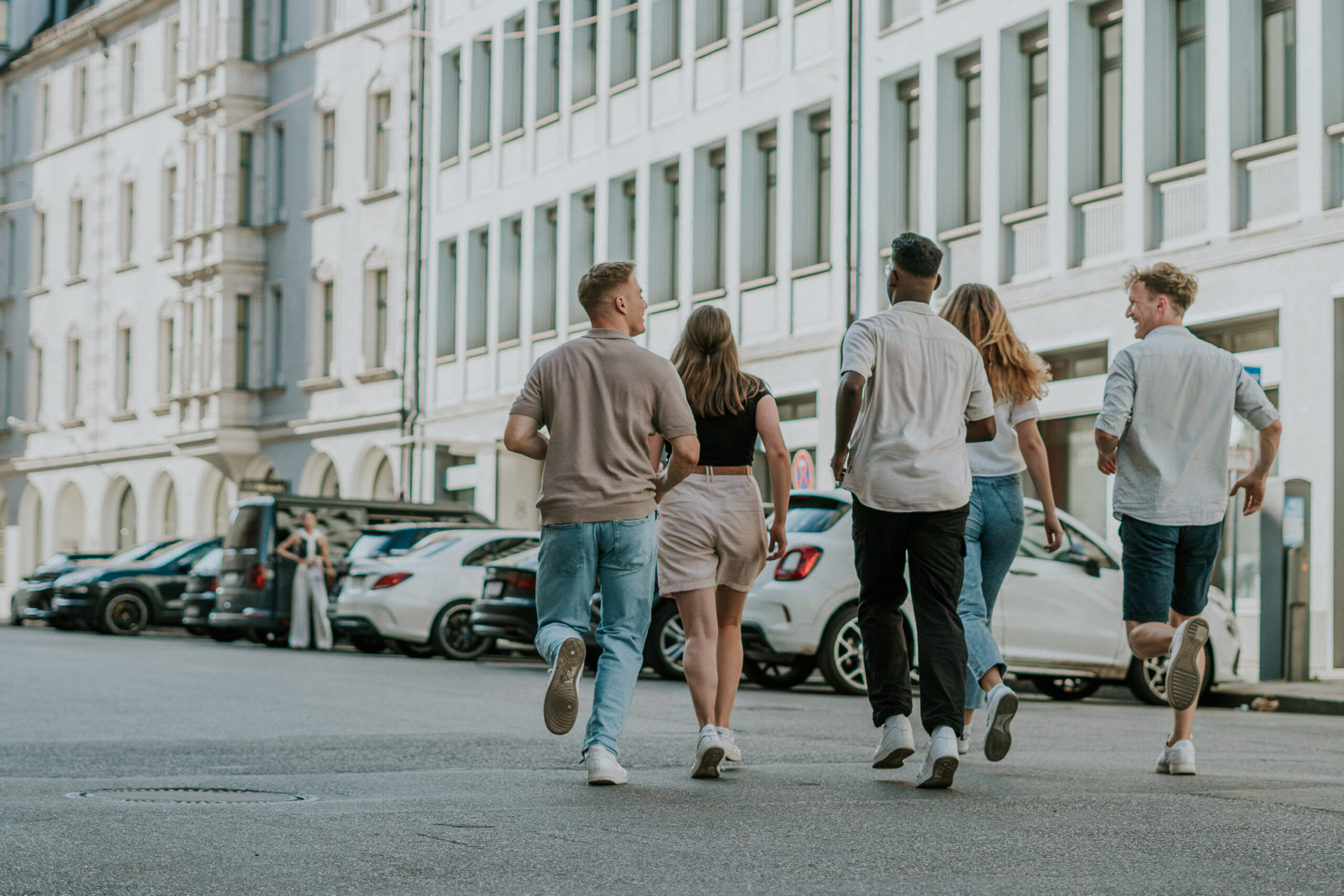 Sechs junge Menschen laufen gemeinsam auf der Straße an einem Gebäude vorbei.
