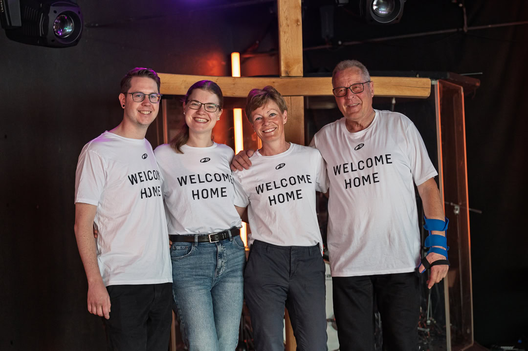 Menschen stehen zusammen, alle tragen T-Shirts mit "WELCOME HOME".