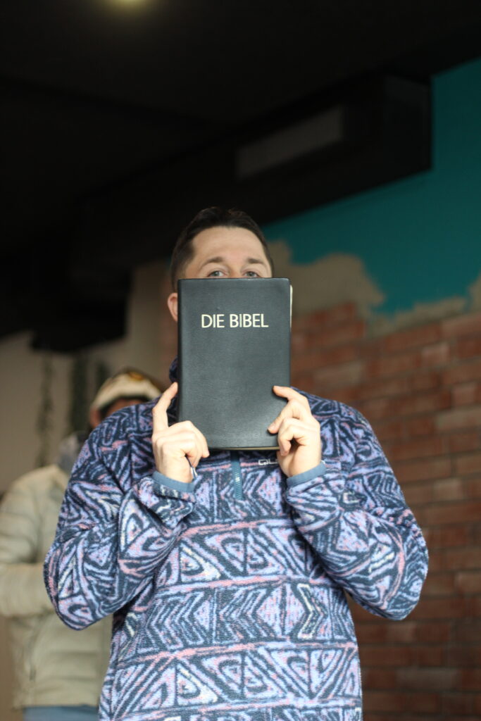 Mann hält ein schwarzes Buch mit "DIE BIBEL" auf dem Cover vor Gesicht.
