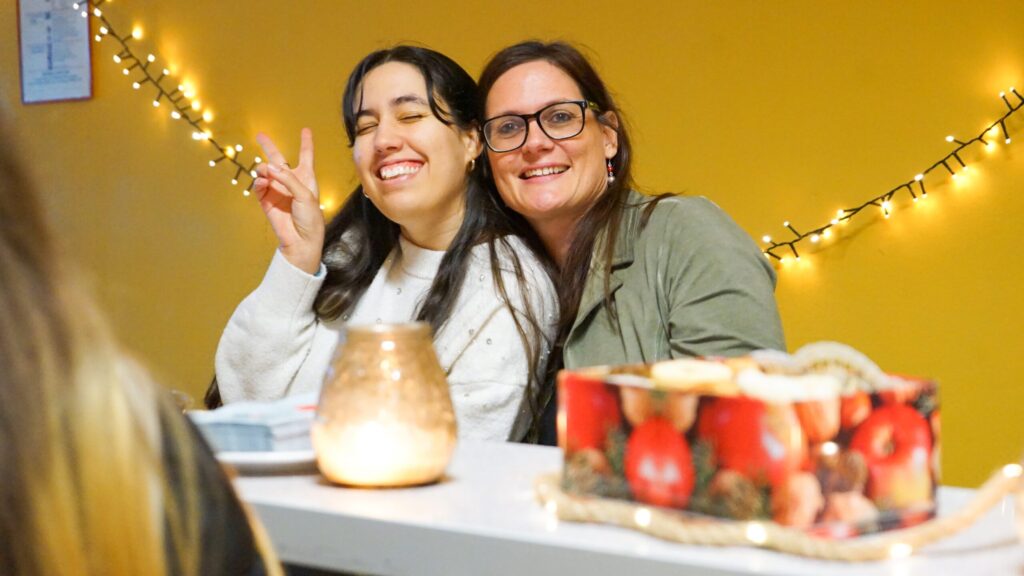 Zwei Frauen sitzen an einem Tisch, lachen und posieren für ein Foto.