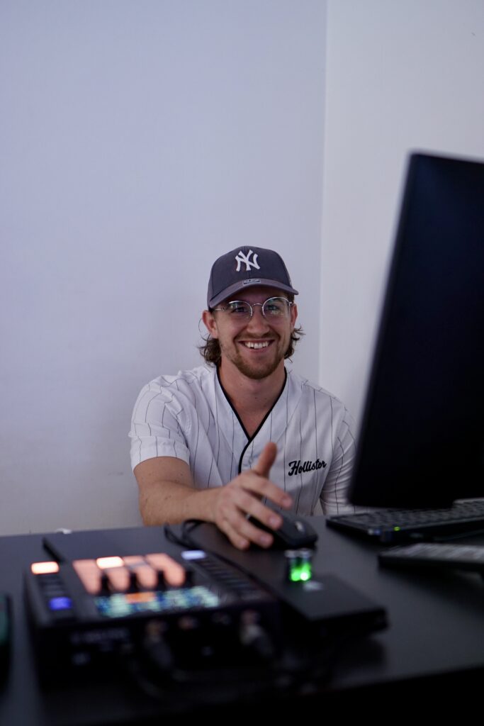 Mann mit Baseballcap und Brille arbeitet an Computer, lächelt.
