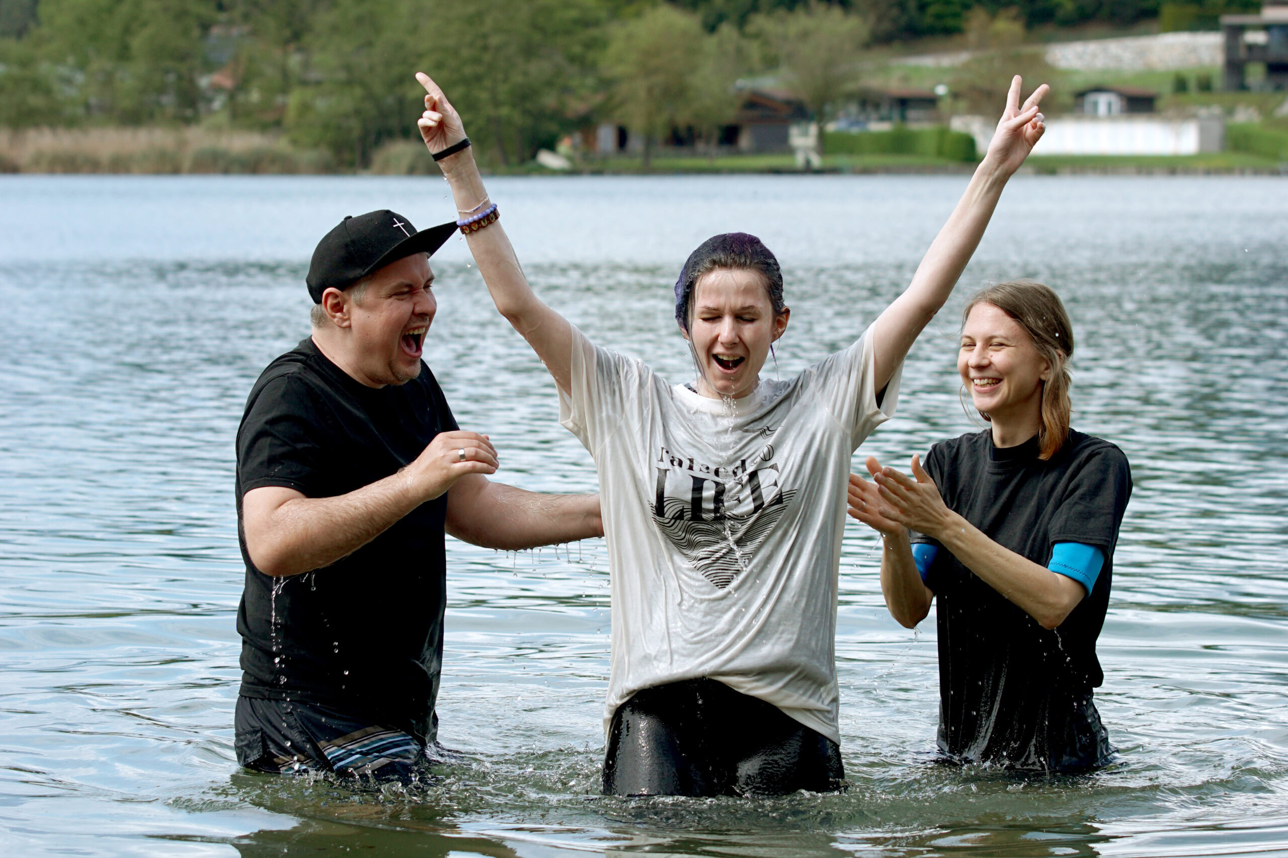 Drei Personen stehen im Wasser, eine Person hebt die Arme, die anderen klatschen.