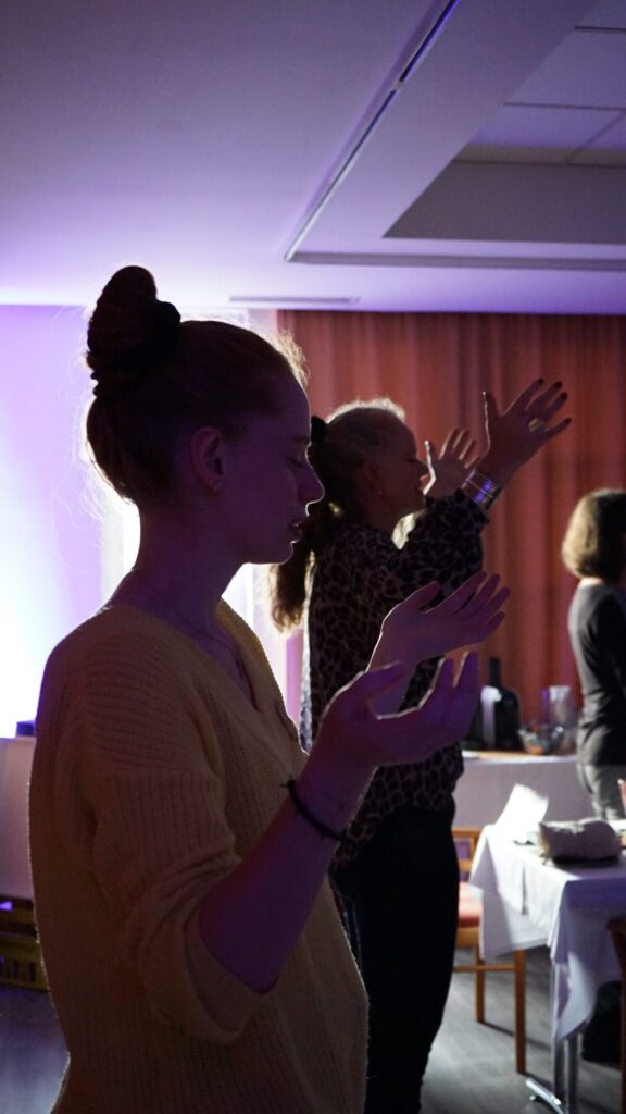 Zwei Frauen mit geschlossenen Augen und erhobenen Händen in einem Raum.