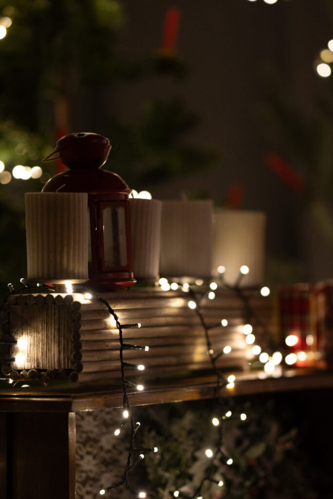Kerzen, Lichterkette und Dekoration auf einem Tisch, im Hintergrund Tannenzweige.