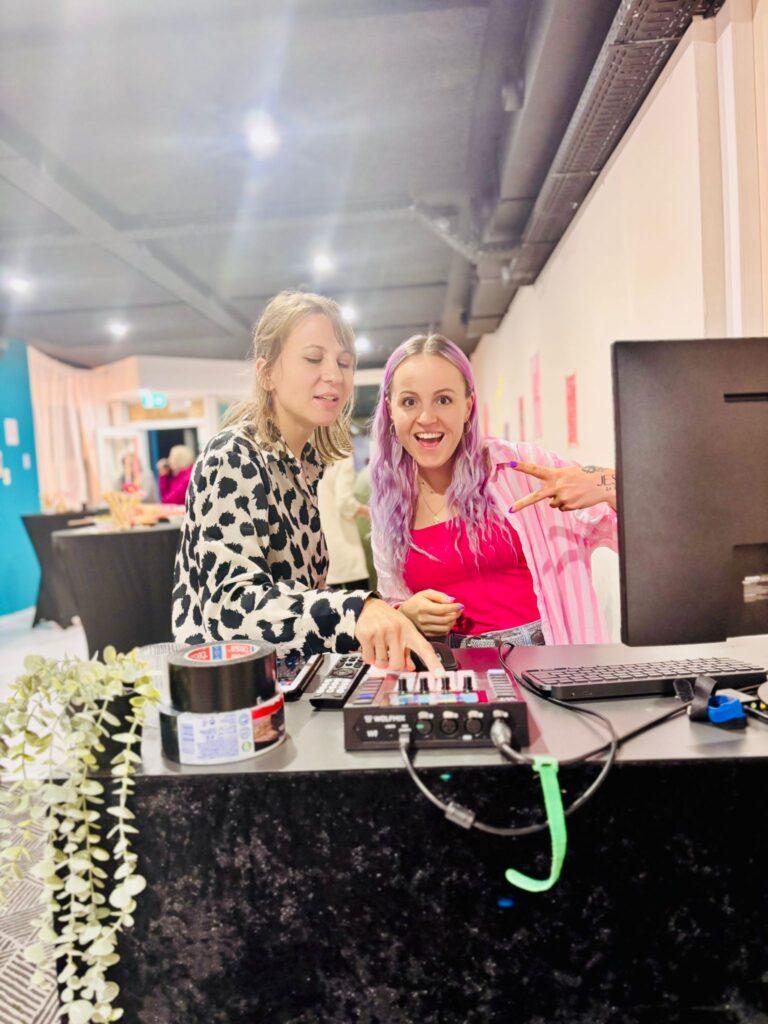 Zwei Frauen arbeiten an einem Computer an einem schwarzen Tisch, eine zeigt auf den Bildschirm.