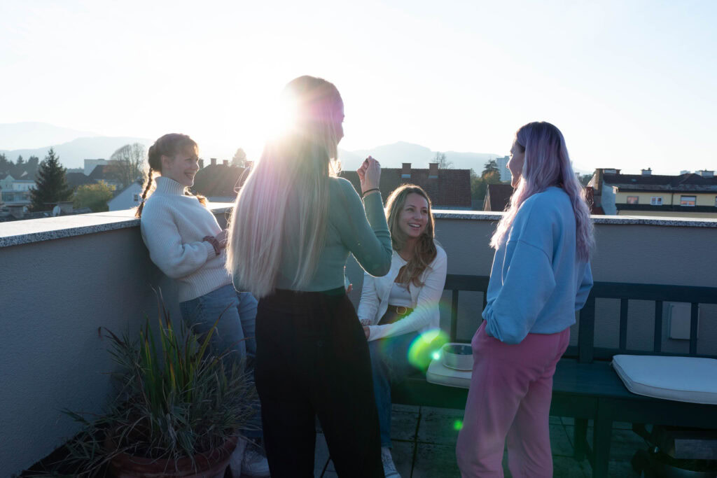 Vier Frauen stehen auf einem Balkon, unterhalten sich, bei Sonnenuntergang.