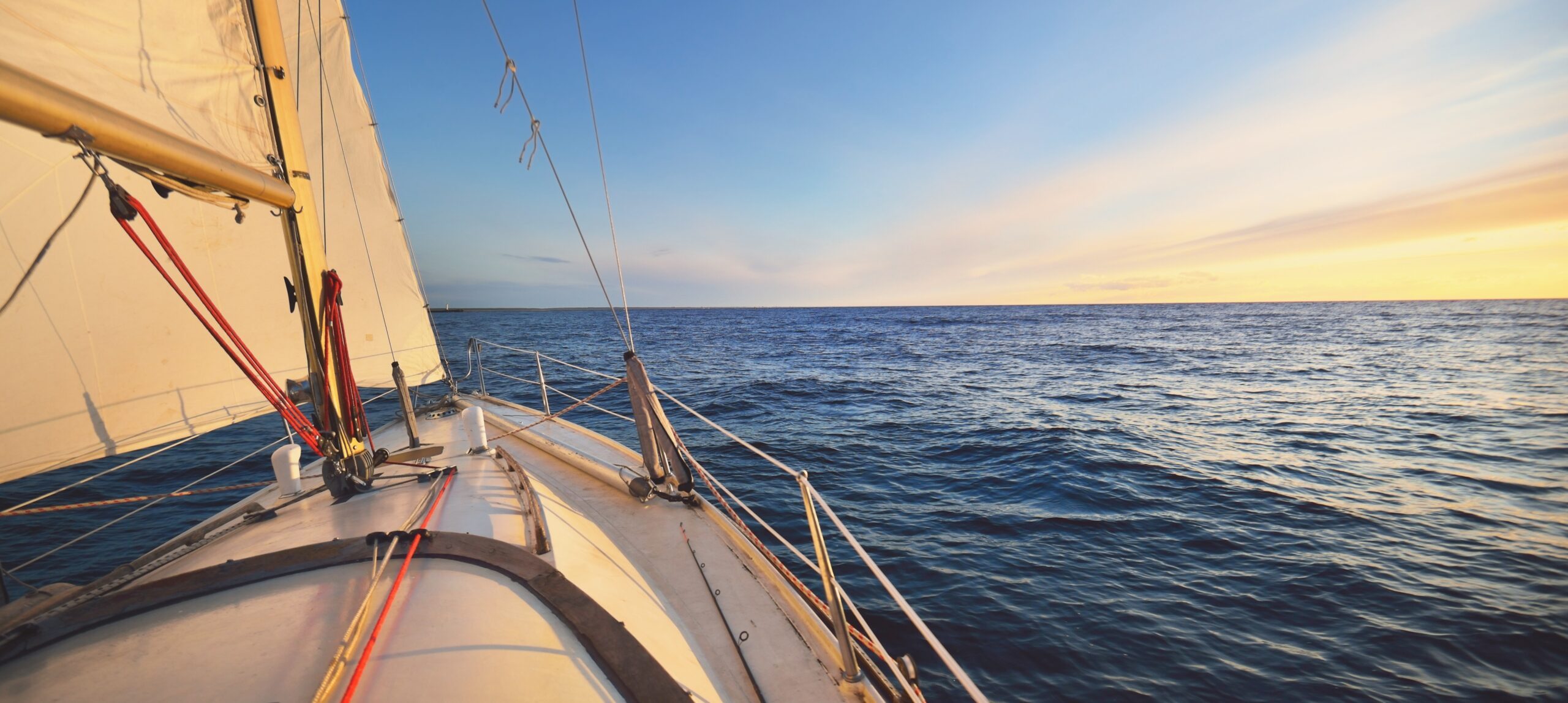 Blick vom Segelboot auf das offene Meer bei Sonnenuntergang, Segel und Ruder sichtbar.