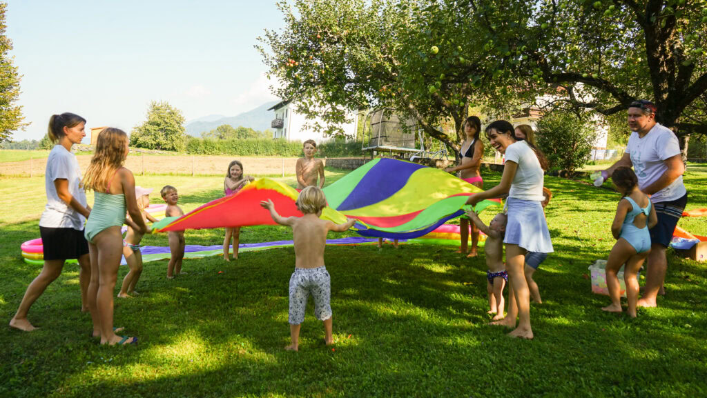 Mehrere Kinder und Erwachsene spielen mit einem bunten Tuch im Garten.
