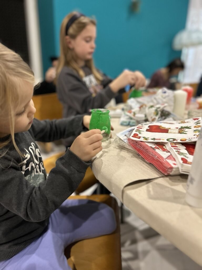 Zwei Kinder sitzen an einem Tisch, eines hält einen grünen Spielzeug-Controller.