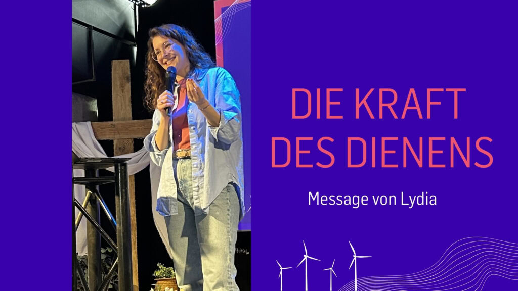 Frau spricht in Mikrofon vor Publikum, hinter ihr ein Bildschirm mit Text.