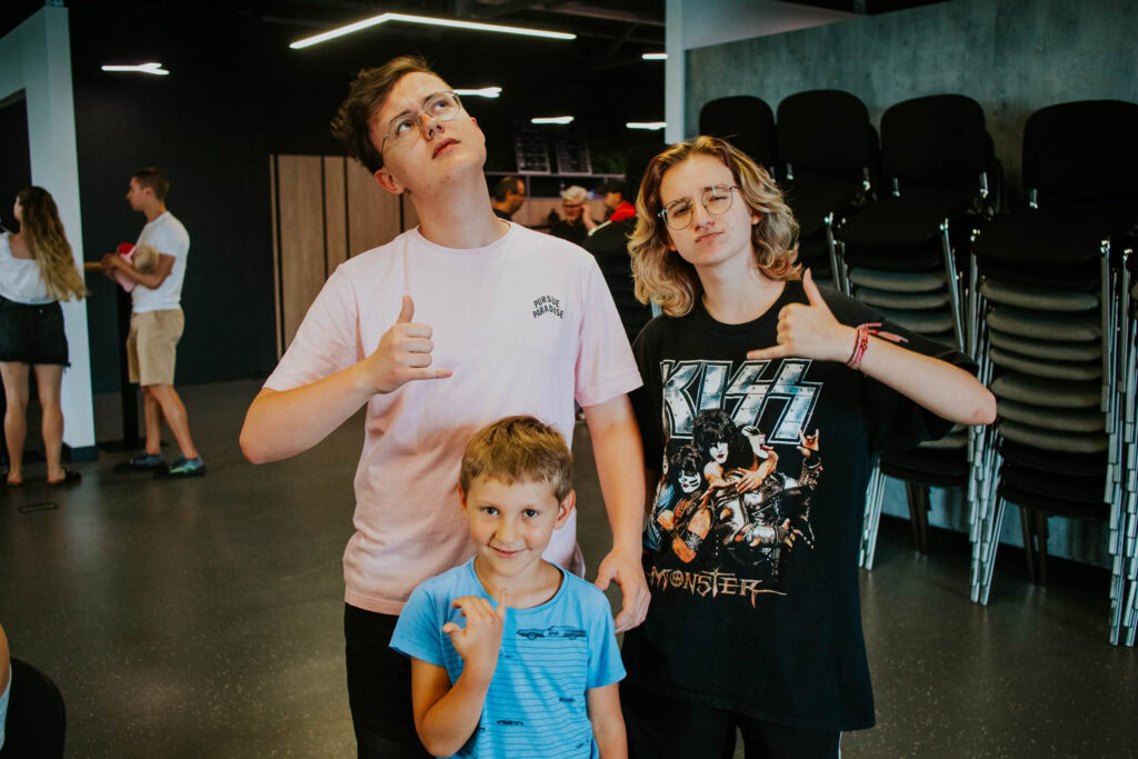 Young man and two children standing indoors, one giving a thumbs-up.