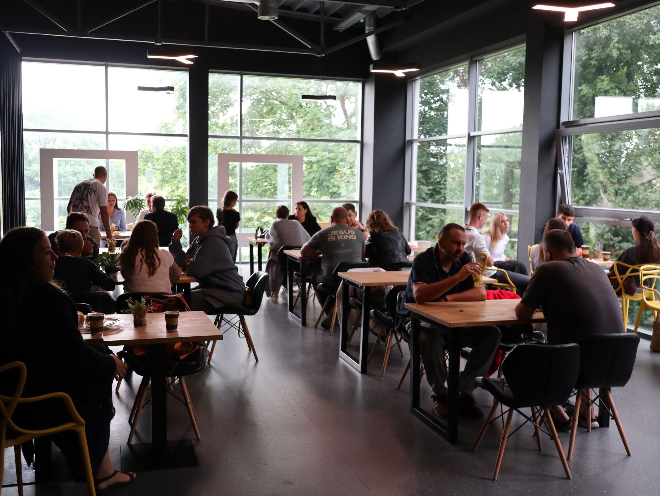 A group of people sitting at tables in a modern co-working space with large windows.