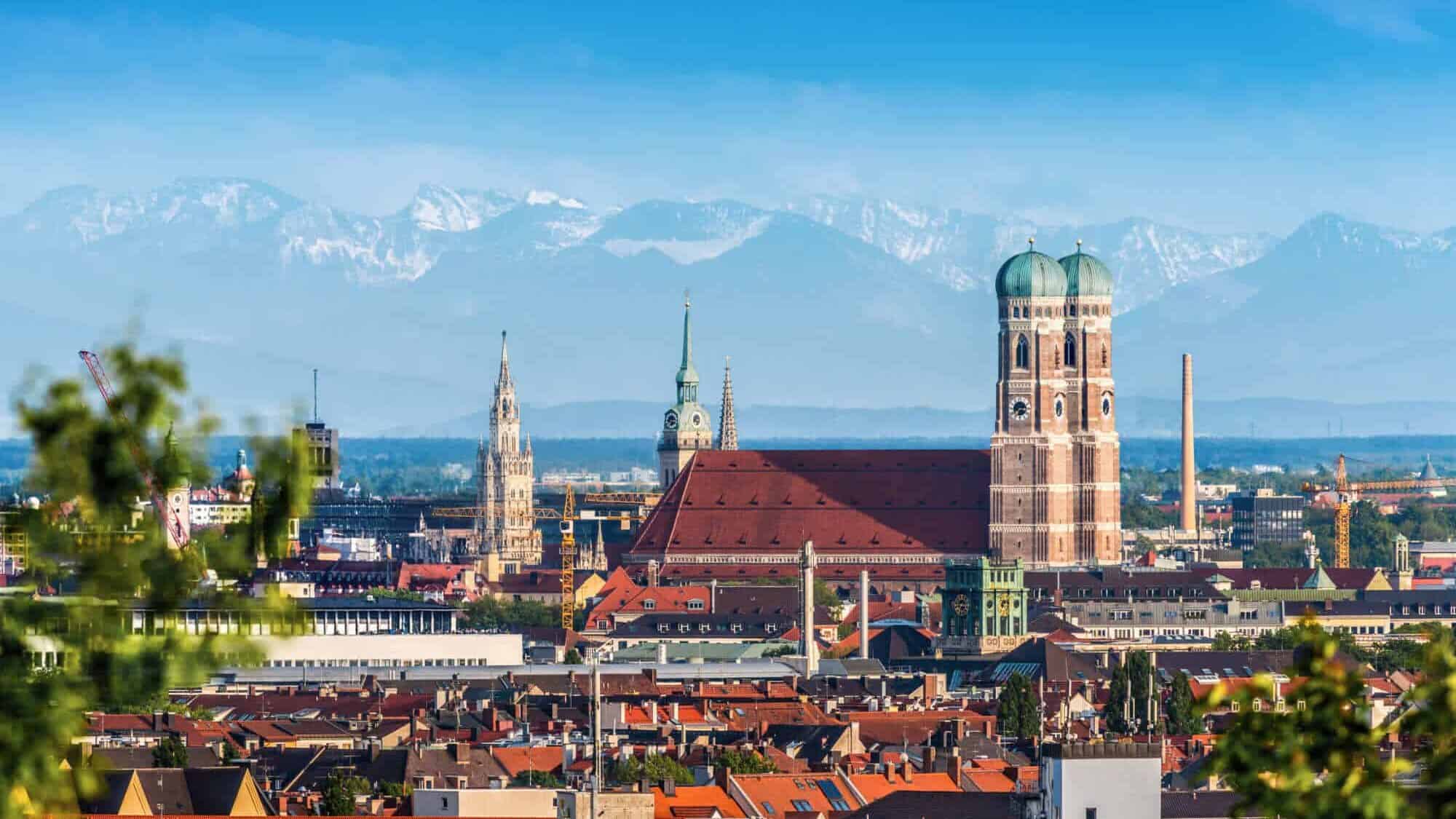 High-quality panoramic photo of Munich with the famous town hall and the Alps in the background, emphasizing the lively city with Bavarian culture and religious tradition.