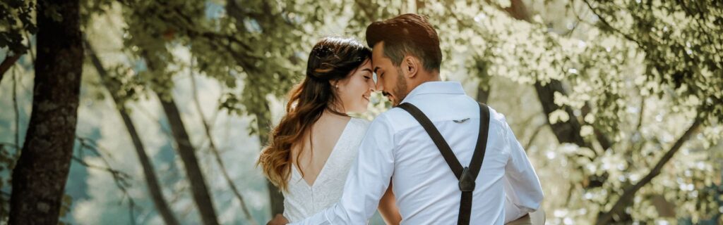 A man and a woman stand facing each other with their heads bowed in a park.
