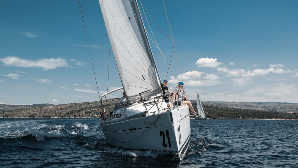 Sailing boat with five people on the sea, blue sky, landscape in the background.