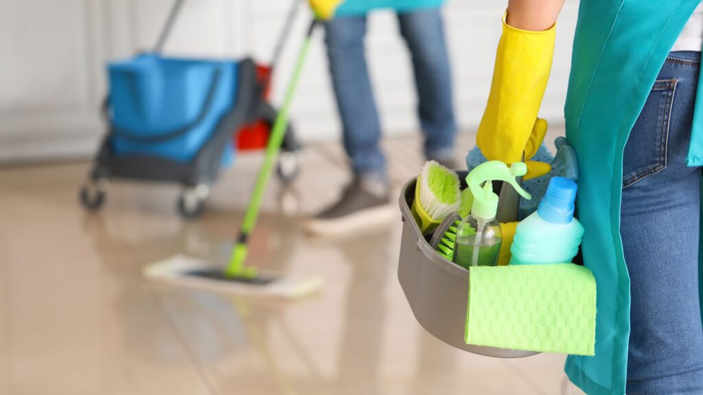 Cleaner holding a bucket with cleaning utensils.