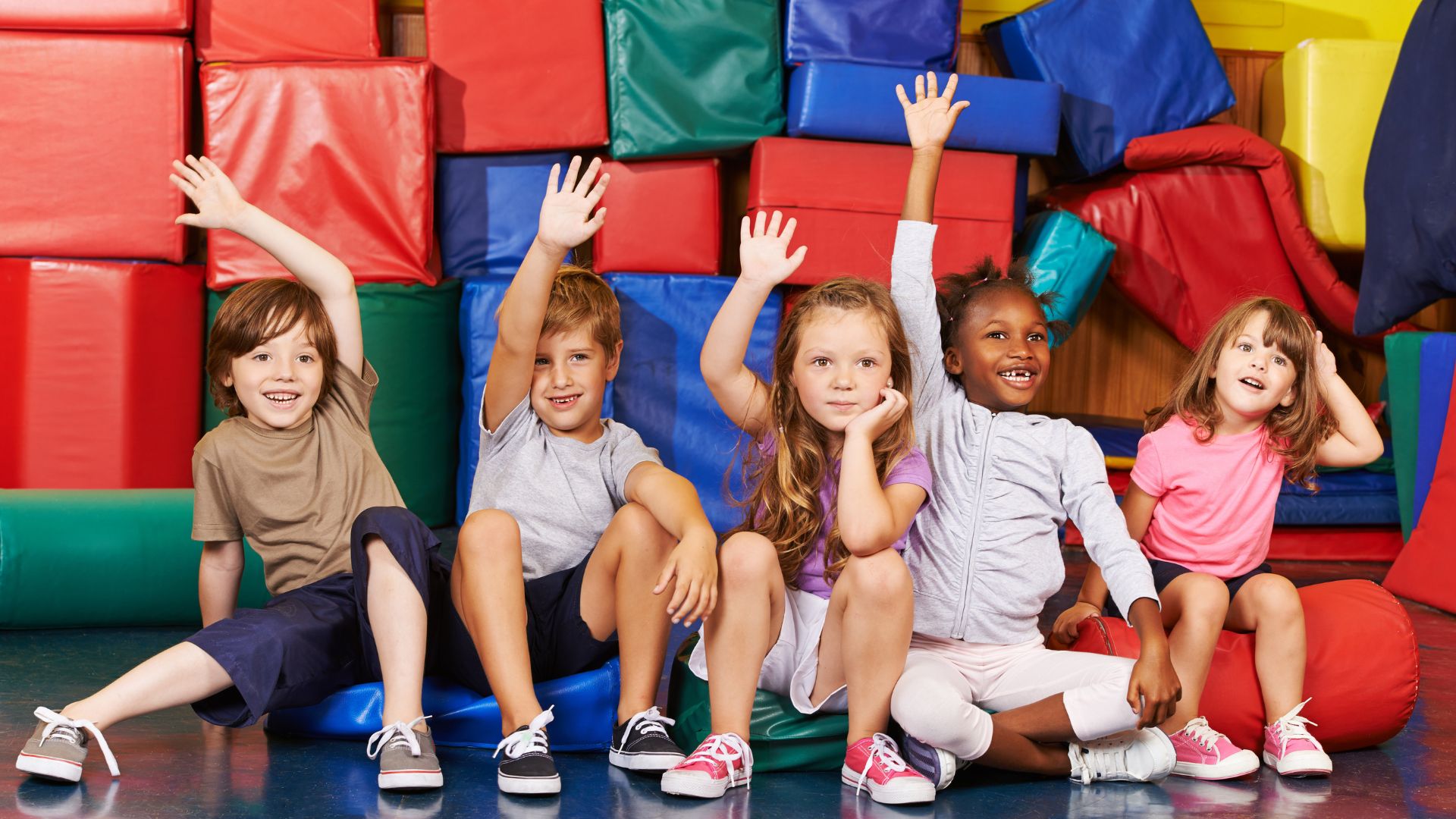 Fünf Kinder sitzen vor bunten Geschenkpaketen, einige winken.