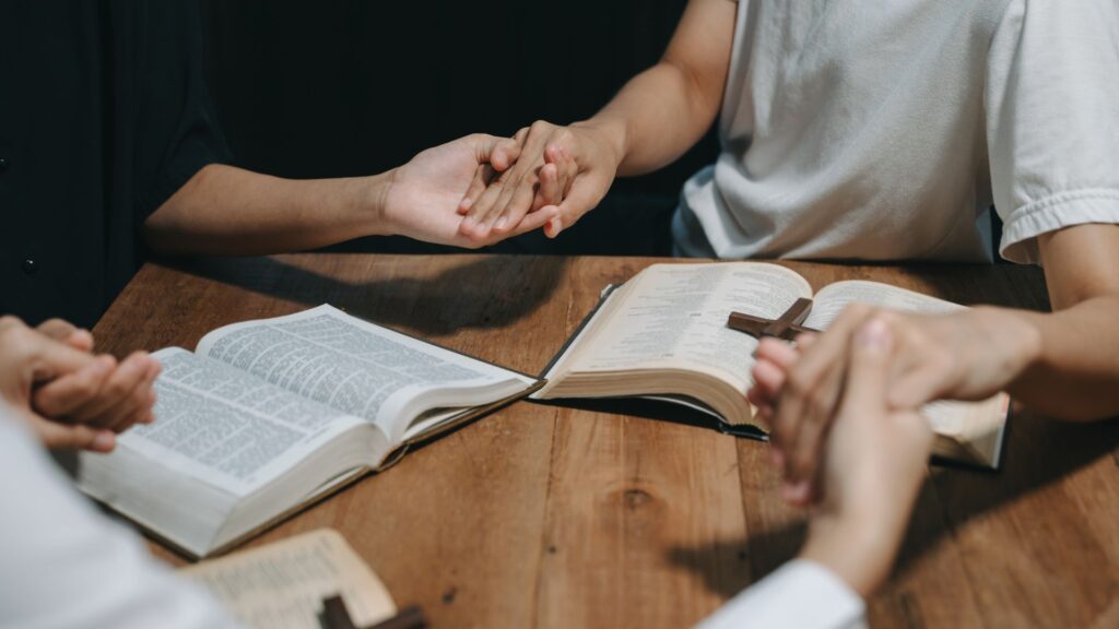 Two people hold hands over open Bibles on a table.