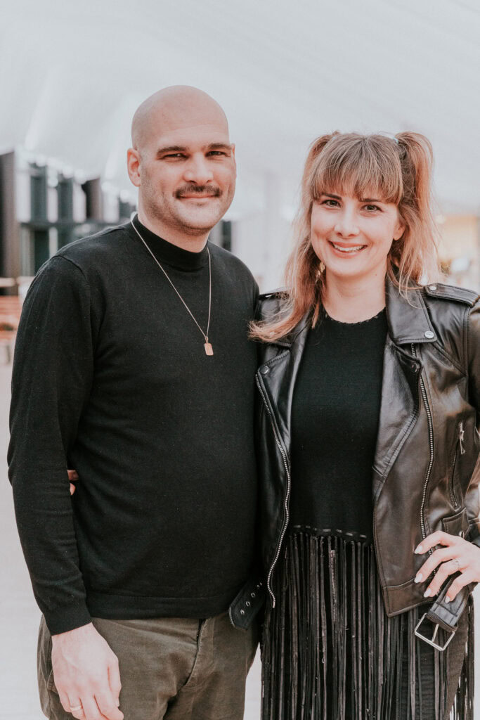 A man and a woman stand next to each other, smiling and posing for the camera.