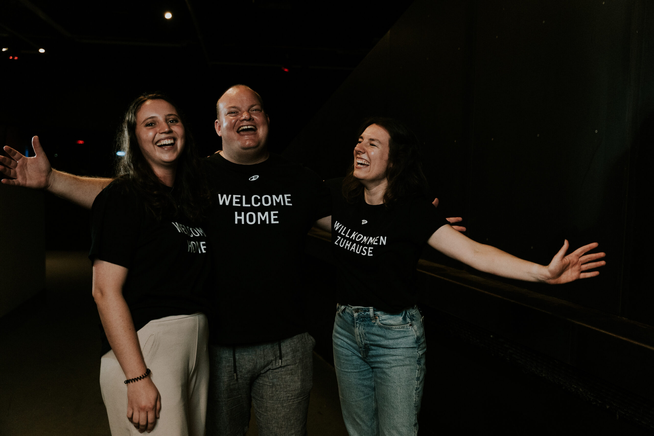 Three people laugh and hug each other in a dark environment.