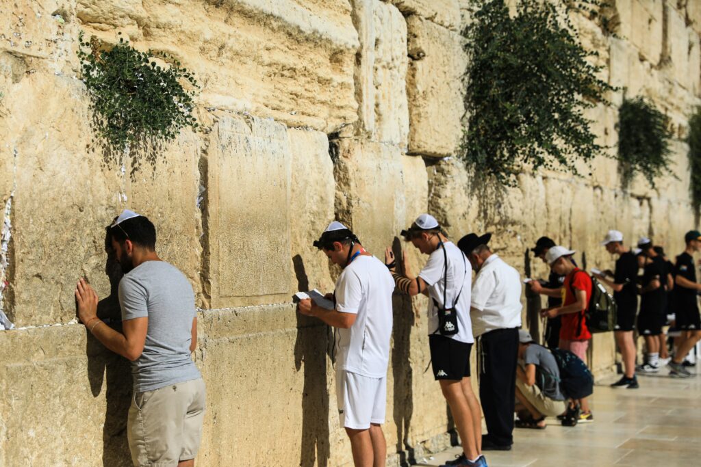 Menschen beten an der Klagemauer, einige stehen mit erhobenem Kopf, andere knien oder berühren die S.
