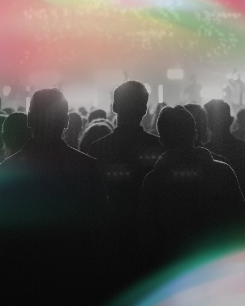 Silhouetten von Menschen vor einer Bühne bei einer Lichtshow.