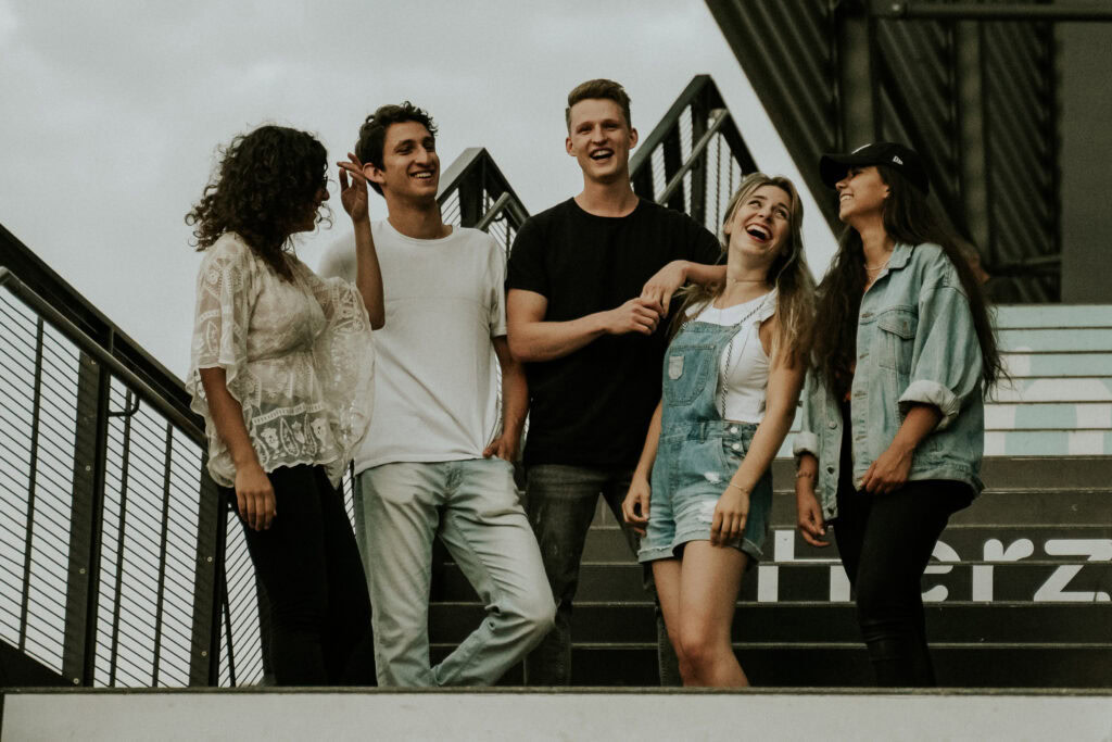 Fünf junge menschen stehen auf einer treppe im freien, lachen und unterhalten sich.