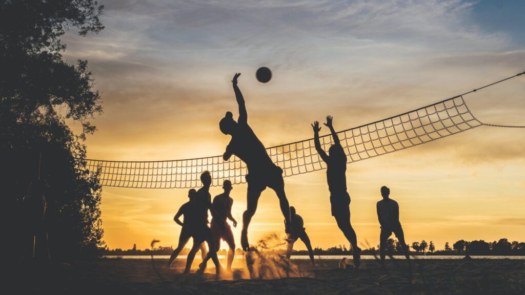 Silhouettes of people playing volleyball on the beach at sunset.