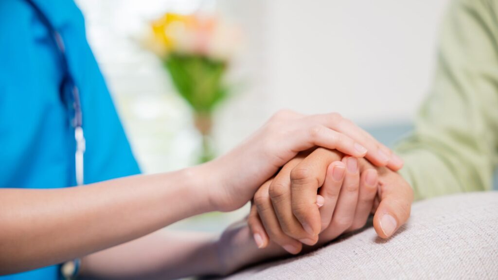 Zwei Personen halten sich an den Händen, eine Person legt die Hand auf die andere.