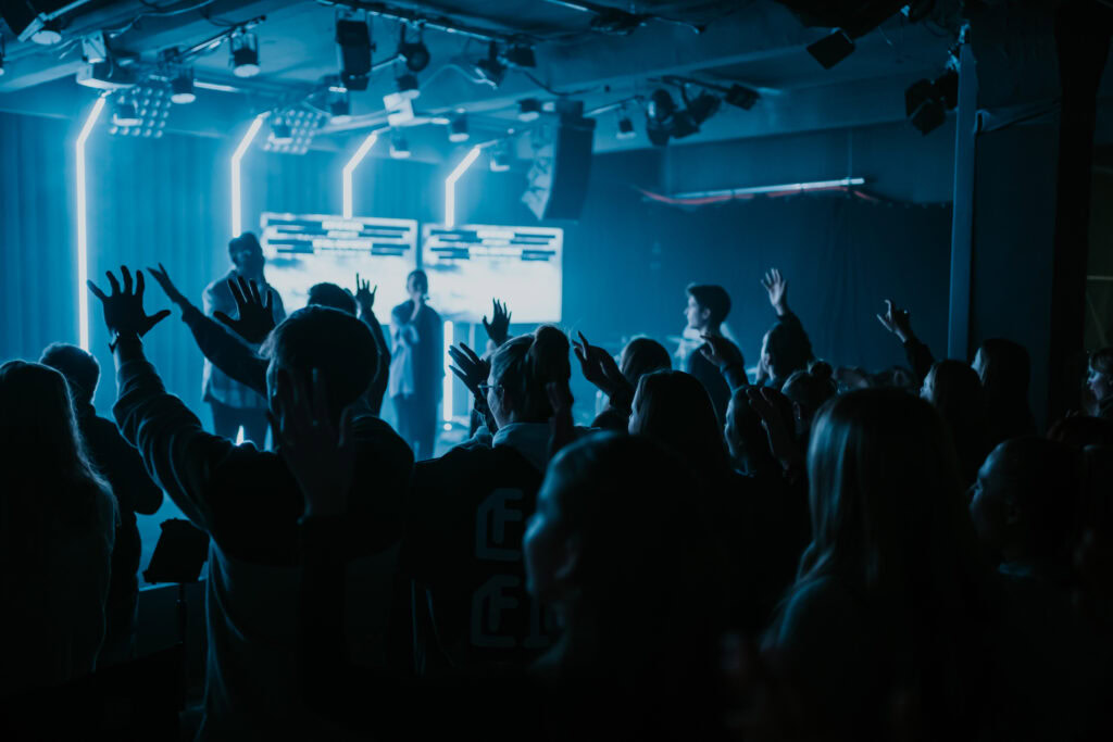 Junge Menschen beim modernen Gottesdienst mit Lichtshow und Musik, die Gemeinschaft und Glauben in einer zeitgemäßen Kirche in Berlin zeigen.