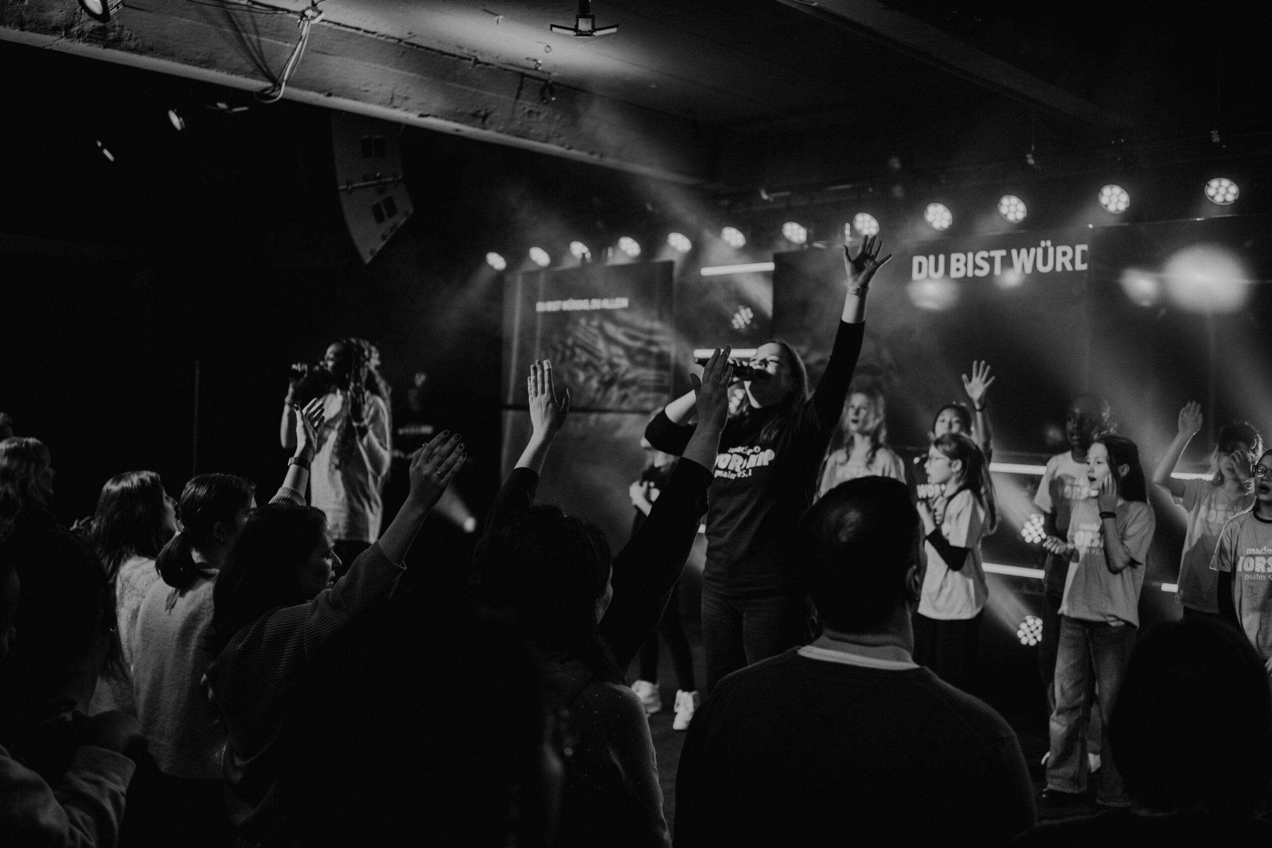 Menschen auf einer Bühne beim Singen und Tanzen, Publikum mit erhobenen Händen.