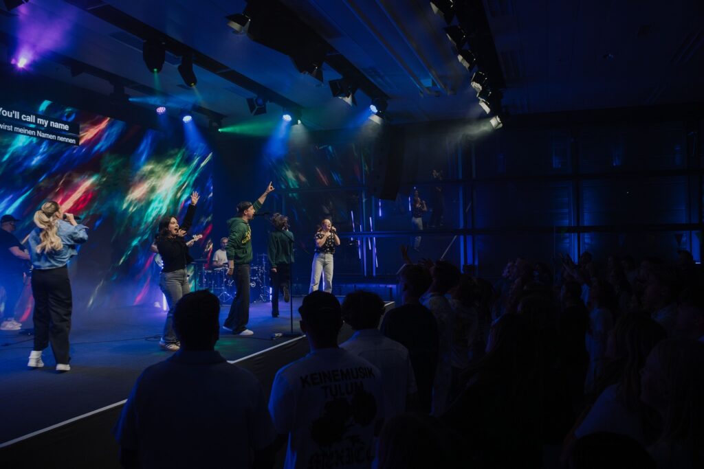 Junge Menschen bei einem dynamischen Gottesdienst im Rahmen von ICF XY in Bern, umgeben von bunter Lichtshow, feiern Gemeinschaft und Glauben in einer modernen kirchlichen Umgebung.