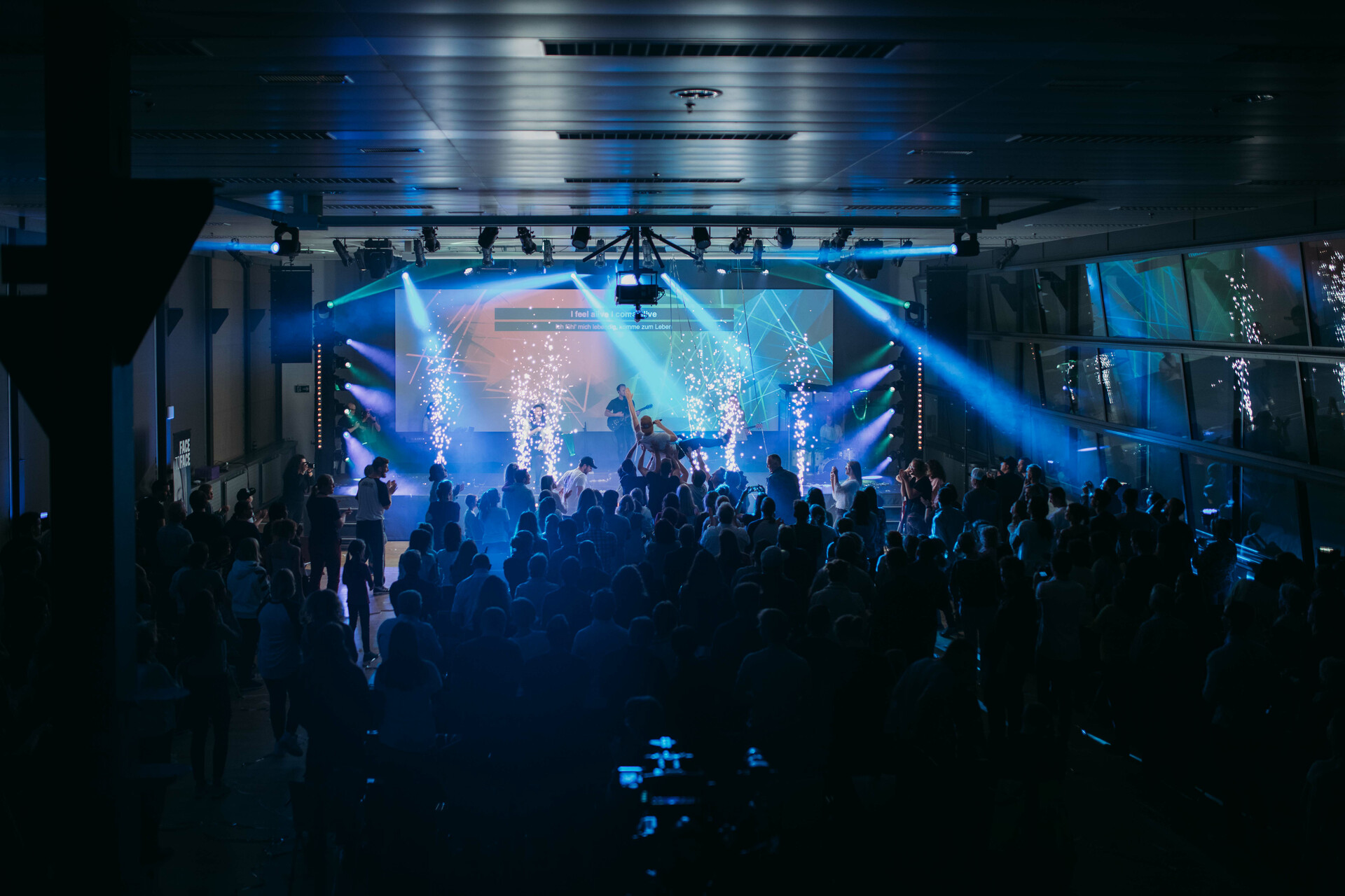 Helles Bild eines modernen Veranstaltungsraums bei ICF Bern mit Bühne, buntem Licht und einer begeisterten Menschenmenge beim Konzert oder einer Veranstaltung.