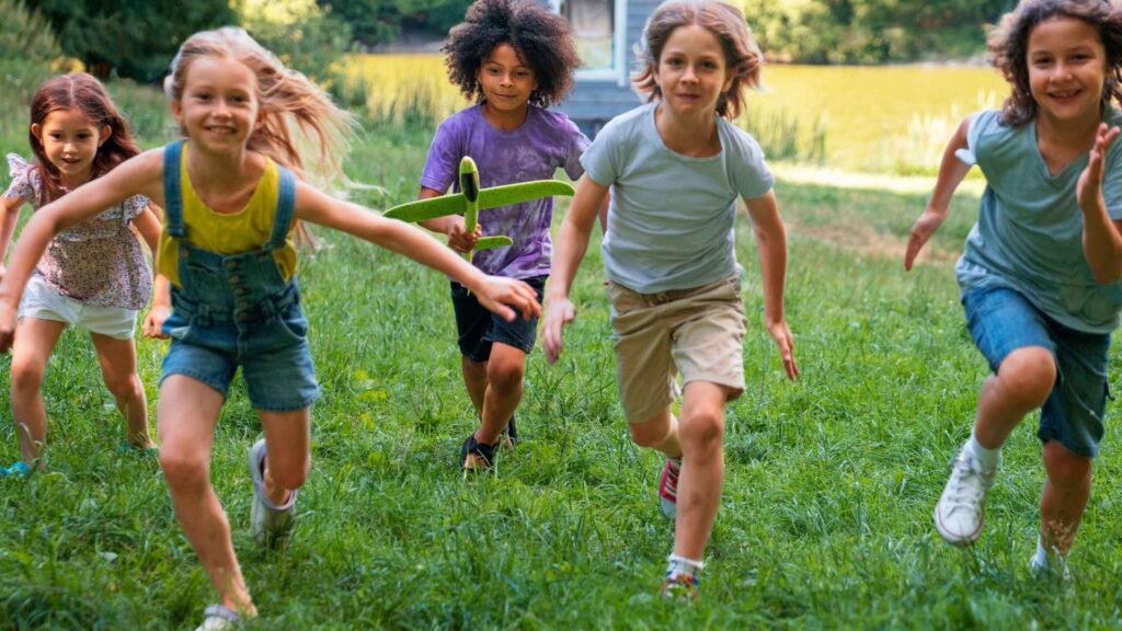 Fröhliche Kinder beim Spielen im Grünen, die gemeinsam draußen Spaß haben und die Natur entdecken. Perfekt für Bilder, die Aktivitäten, Gemeinschaft und Kinderspaß bei ICF Bern präsentieren.