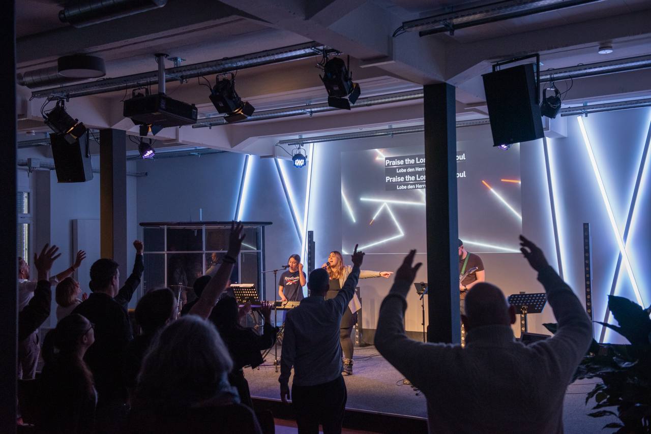 Menschen im Publikum heben die Hände, während eine Band auf der Bühne spielt.