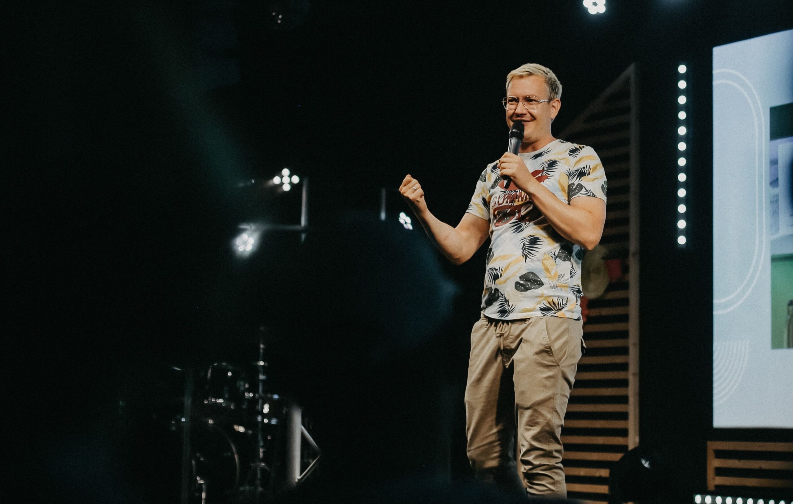 Pastor steht auf der Bühne und predigt mit einem Mikrofon in der Hand