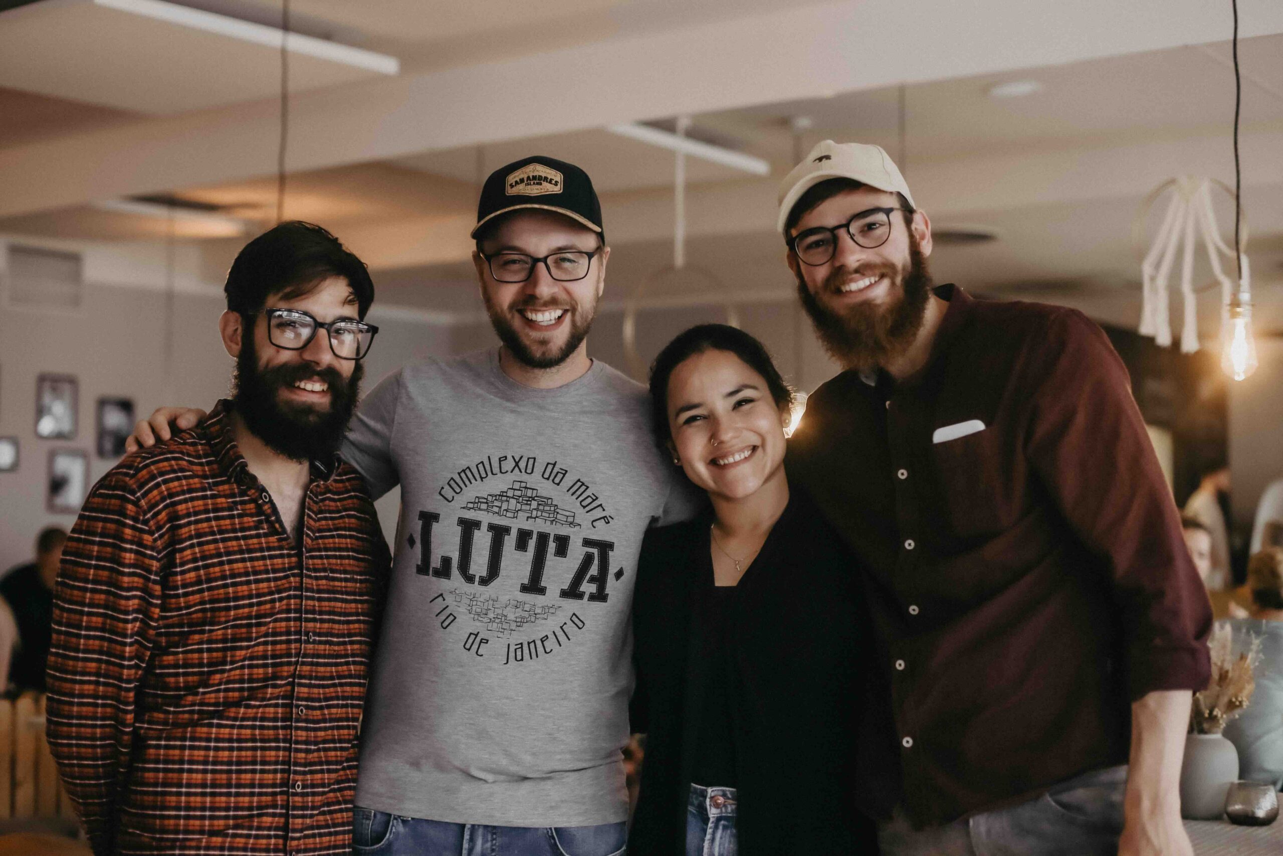 4 junge Personen stehen in einer Reihe und umarmen sich und schauen fröhlich in die Kamera