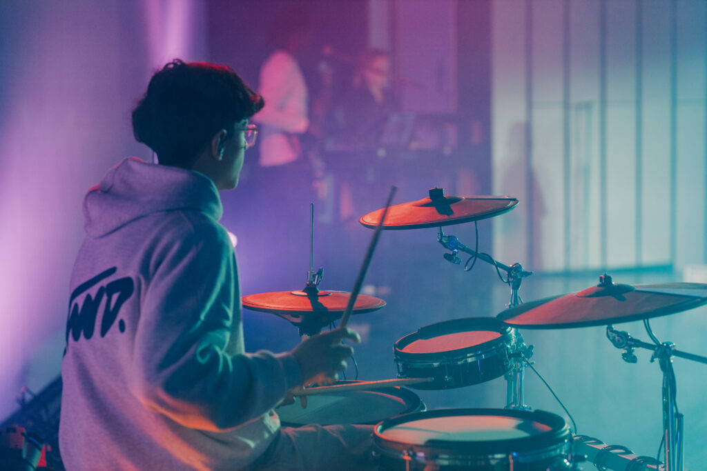 Junge Person spielt Schlagzeug bei einer Live-Musikveranstaltung in der ICF Hamburg Kirche, umgeben von buntem Licht und einer inspirierenden Atmosphäre.