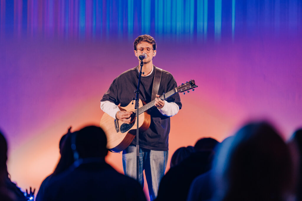 Musiker bei einem Live-Gottesdienst in der ICF Hamburg Kirche, singend und Gitarre spielend vor einer Gemeinde.