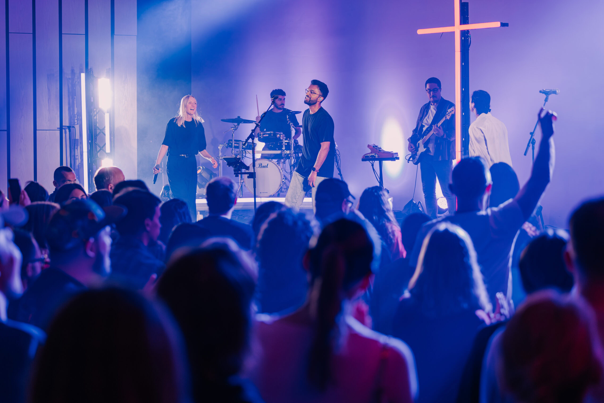 Junge Musiker und Sänger beim Live-Gottesdienst in Hamburg, mit einer großen Gemeinde im Hintergrund, beleuchtet mit bunten Lichtern.