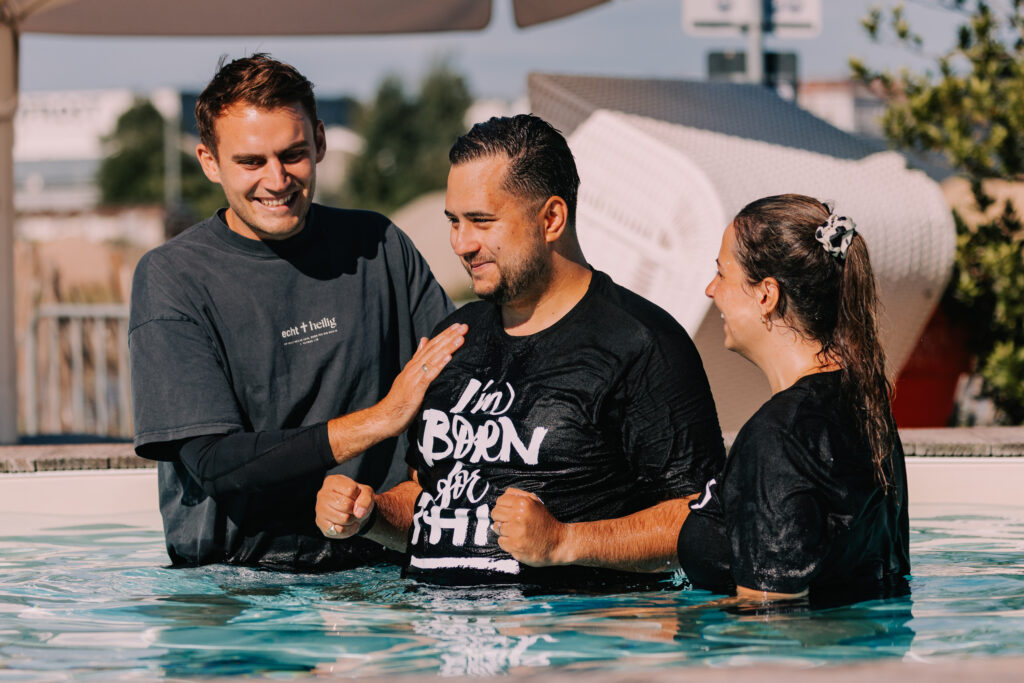 Drei Menschen im Wasser bei einer religiösen Zeremonie, die Gemeinschaft und Glauben symbolisiert, mit Fokus auf christliche Taufe und spirituelle Erneuerung.