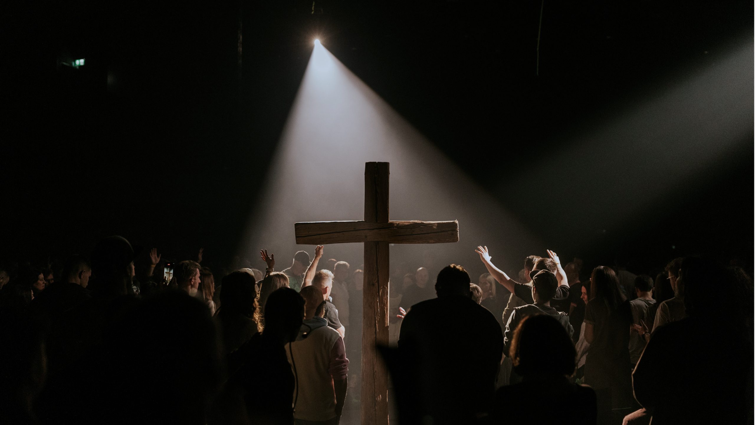 Menschenmenge umkreist ein großes Kreuz, das im Scheinwerferlicht steht.